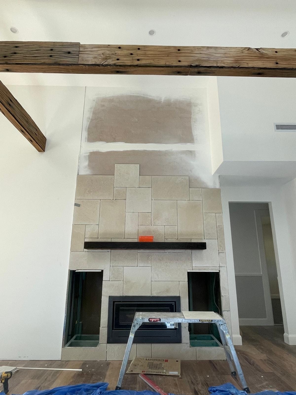 The first courses laid around the firebox and alcoves, the upper chimney breast still bare plasterboard, timber beams crossing the ceiling above.