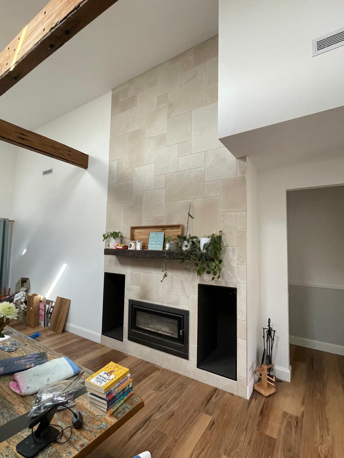 The finished surround in the room it belongs to: trailing plants along the timber mantel, fire lit below, raked ceiling and exposed beams above.