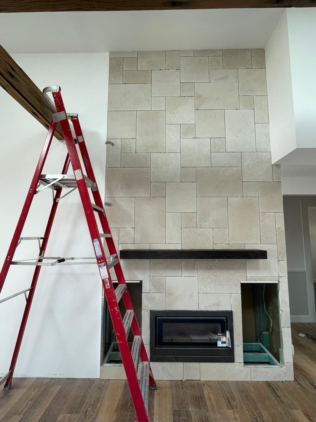 The surround part-tiled, the random ashlar pattern set out course by course up the chimney breast with a ladder still against the plasterboard beside it.