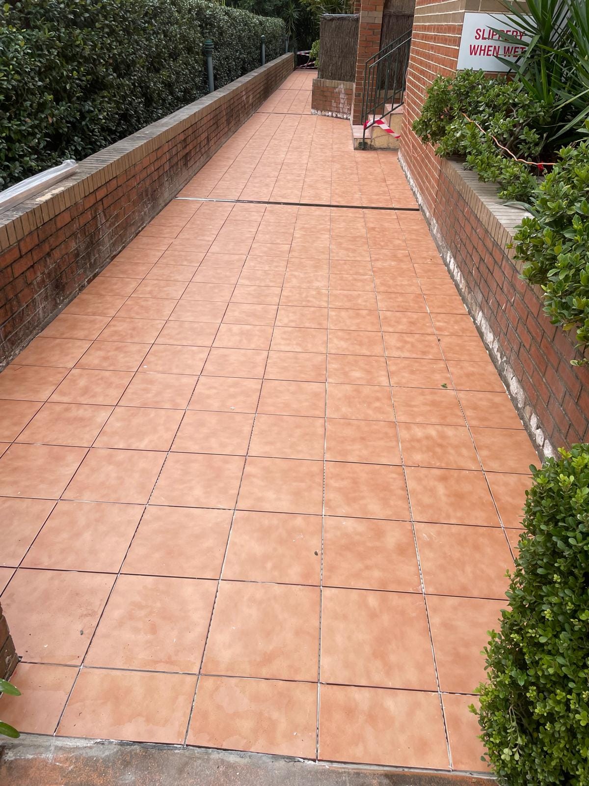 A long external walkway laid in terracotta, grout lines running dead straight down its full length