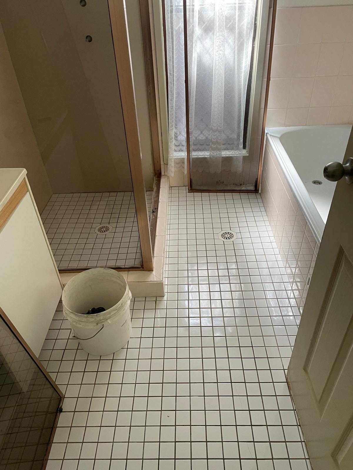 Looking down at the original white mosaic floor with its round chrome waste, the stepped shower hob and the bath returning along the far wall.