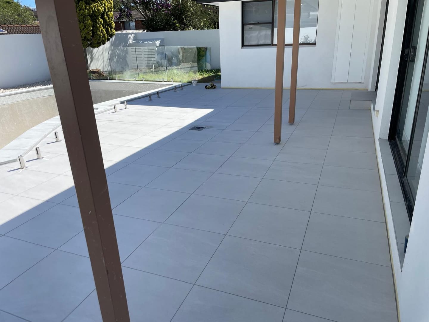 The terrace running back under the alfresco roof to the house, joints aligned the full distance and a drain set flush at the transition.