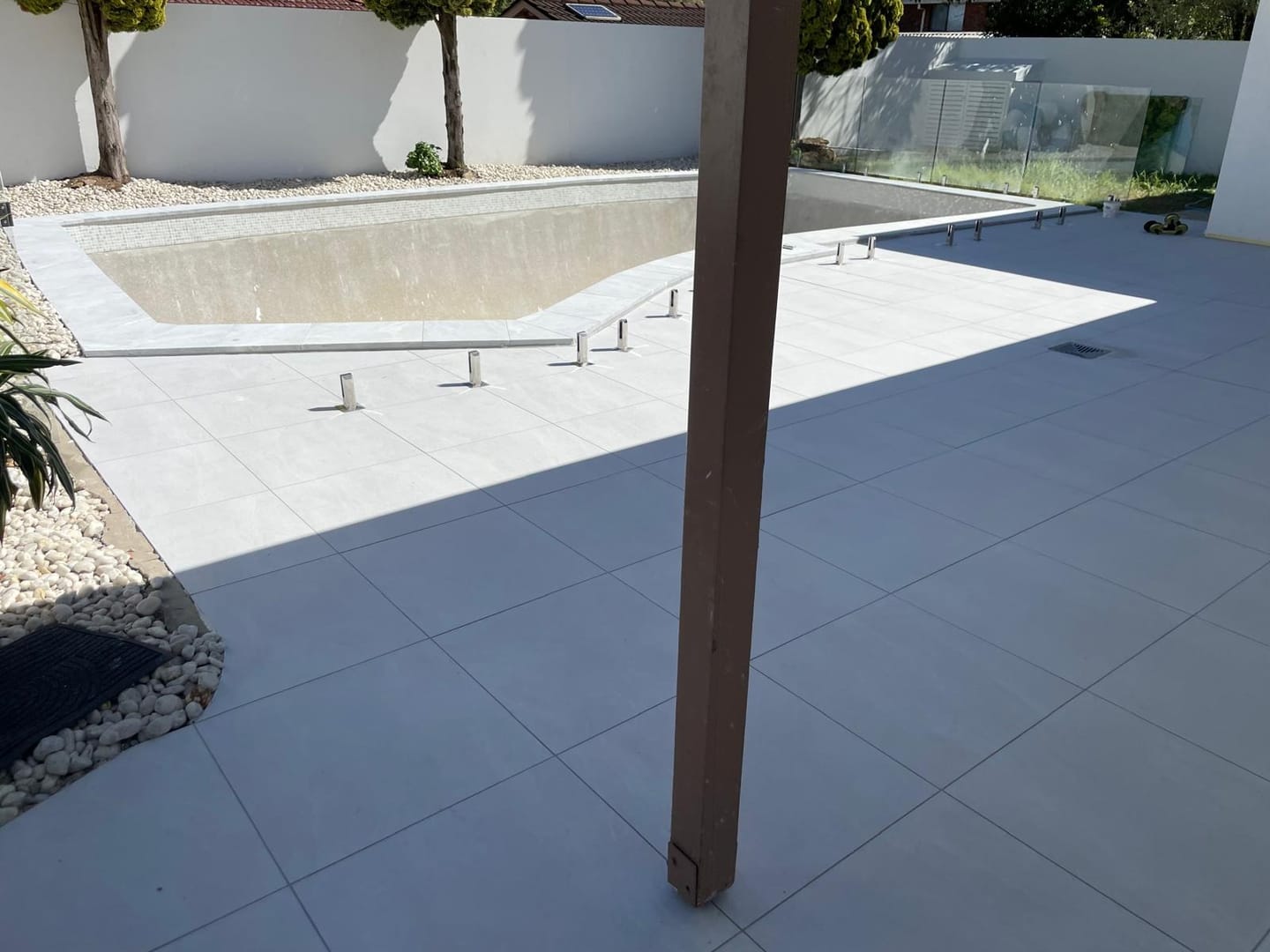 The finished surround meeting the pool coping, tiles cut to follow the curve of the shell and a square grate set flush into the field.