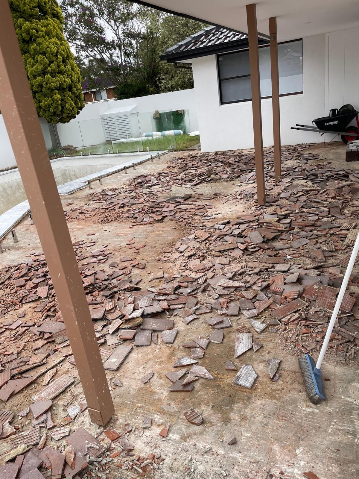 Demolition underway across the whole pool surround, old pavers broken up where they lay and swept into windrows ready to be carted out.