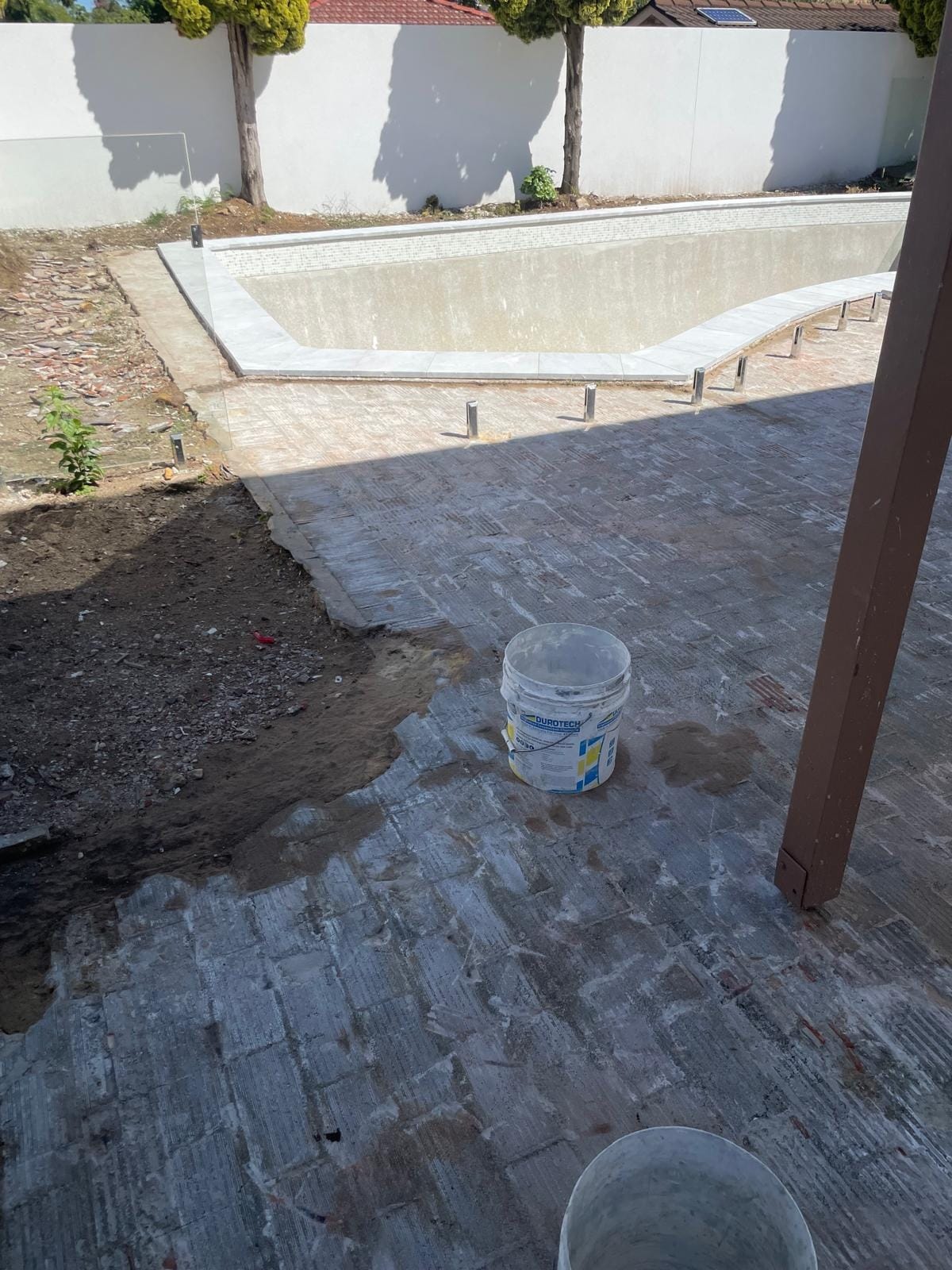 The surround taken back to the old bedding mortar and swept, pool coping already relaid in pale stone, waterproofing on site ready to go down.