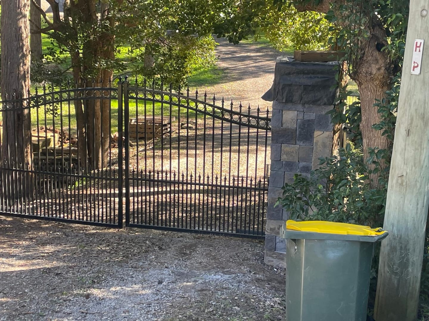 A single clad pier carrying the hinge side of the wrought iron gate, stone returned around the full face, gravel drive running past into the trees.